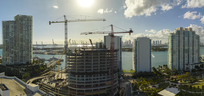 Aerial view of new developing residense in american urban area. Tower cranes at industrial construction site in Miami, Florida. Concept of housing growth in the USA